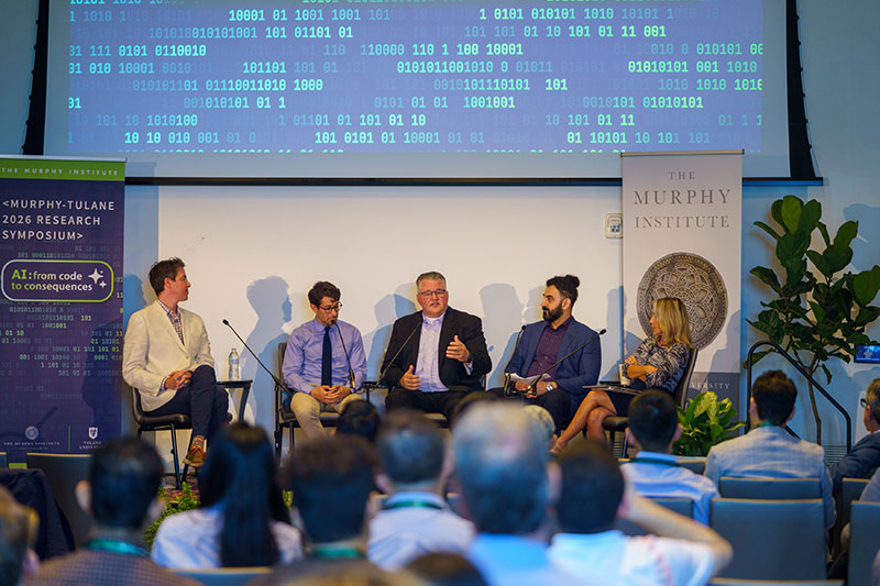Panel discussion with five people on stage in front of a screen with code.