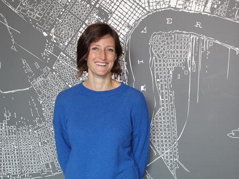 Johanna Nice in a blue sweater smiles in front of a city map graphic.