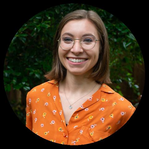 Caroline Leffert, a young woman with glasses smiles in an orange floral shirt outdoors.