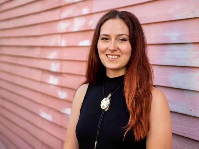 Kaylie McCarthy, a woman with red hair smiling in front of pink siding