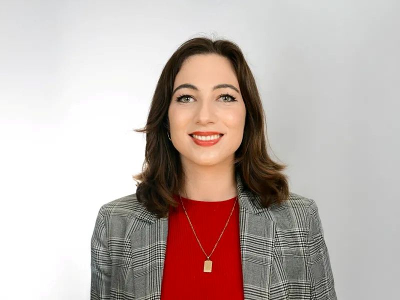 Portrait of a smiling woman in a gray plaid blazer and red shirt.