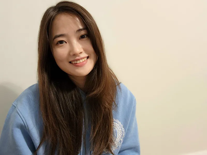 Pureum Lee, young woman with long brown hair wearing a blue hoodie, smiling.