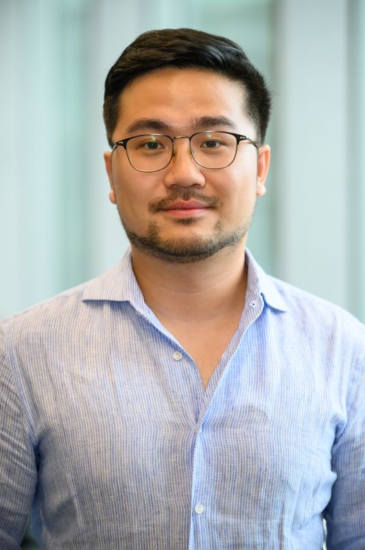 A man with glasses wearing a blue collared shirt looks at the camera.