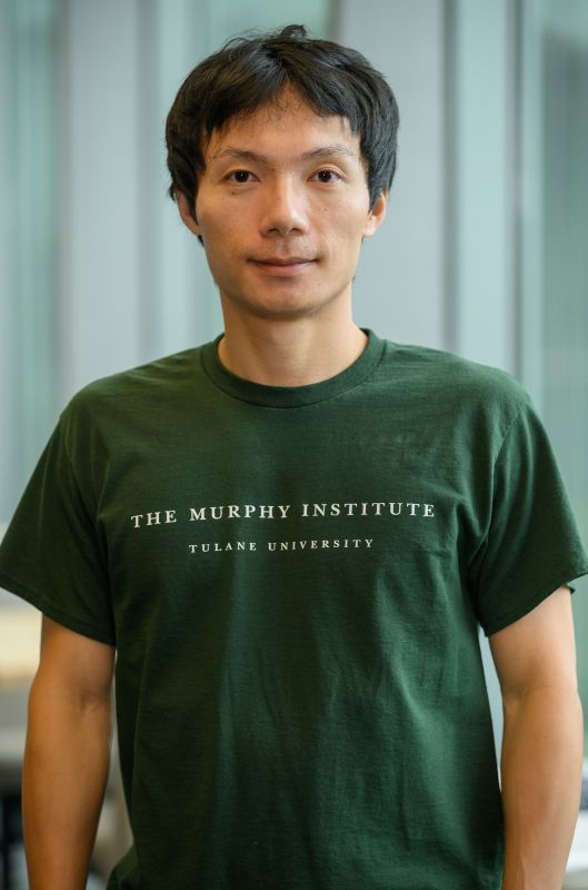 Man wearing a dark green t-shirt with "The Murphy Institute Tulane University" printed on it.