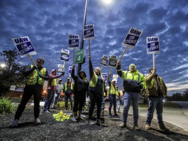 UAW workers holding signs up against an evening sky