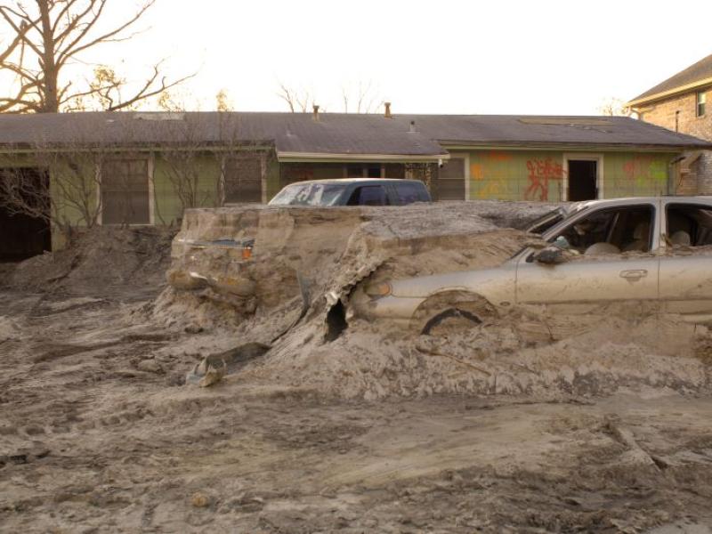 cars embedded in debris and a house damaged by Hurricane Katrina's levee breach 