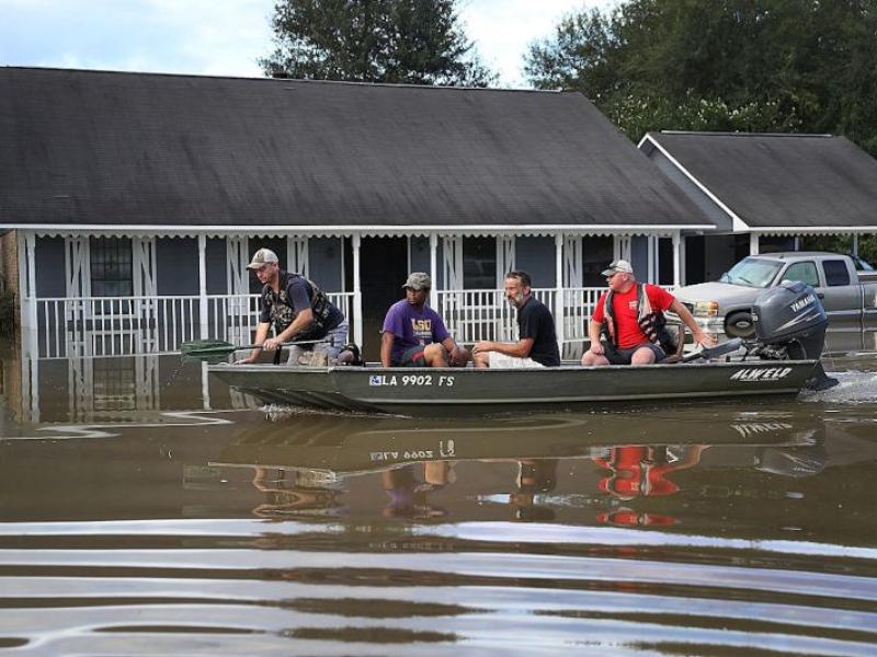 ichard Schafer navigates a boat past a flooded home in Baton Rouge on Aug. 15, 2016