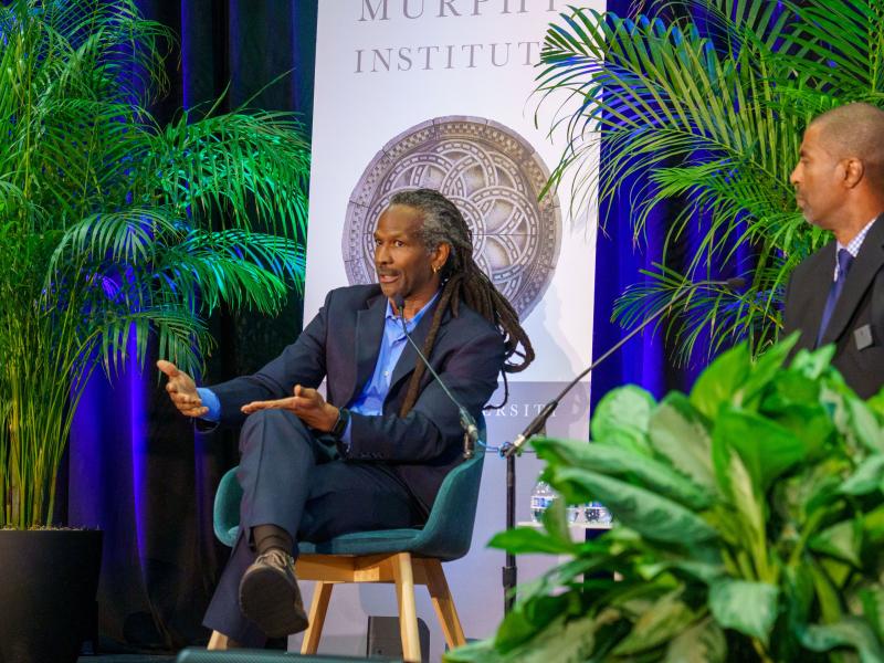 Dr. Carl Hart speaking at the Center for Ethics Fall 2025 Public Lecture seated next to Executive Director Gary "Hoov" Hoover suit