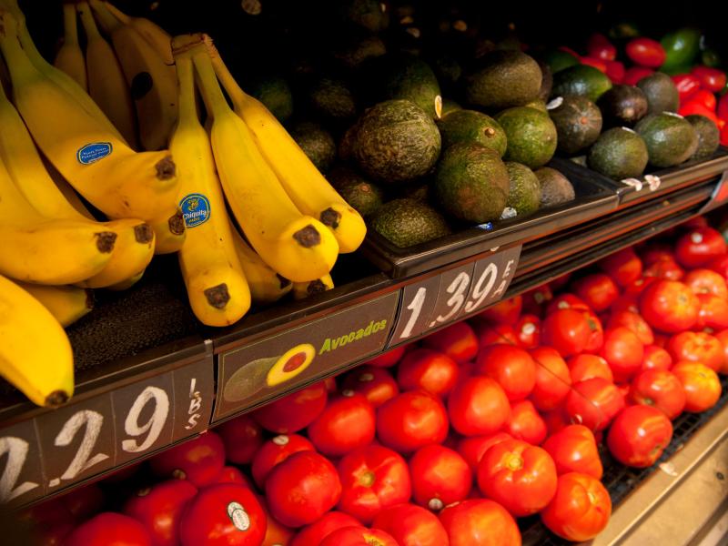 Bananas, avocados, and tomatoes on display at a grocery store with prices listed.