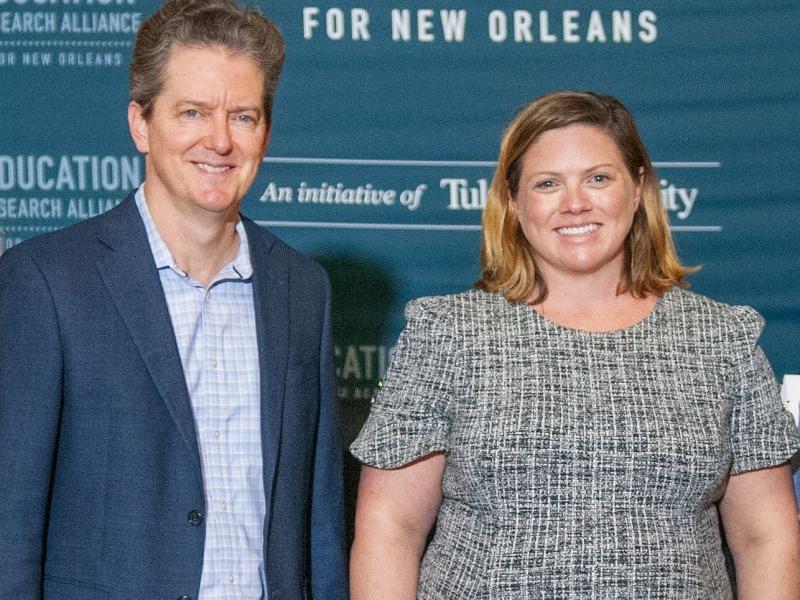Man in suit and woman in patterned dress smile.