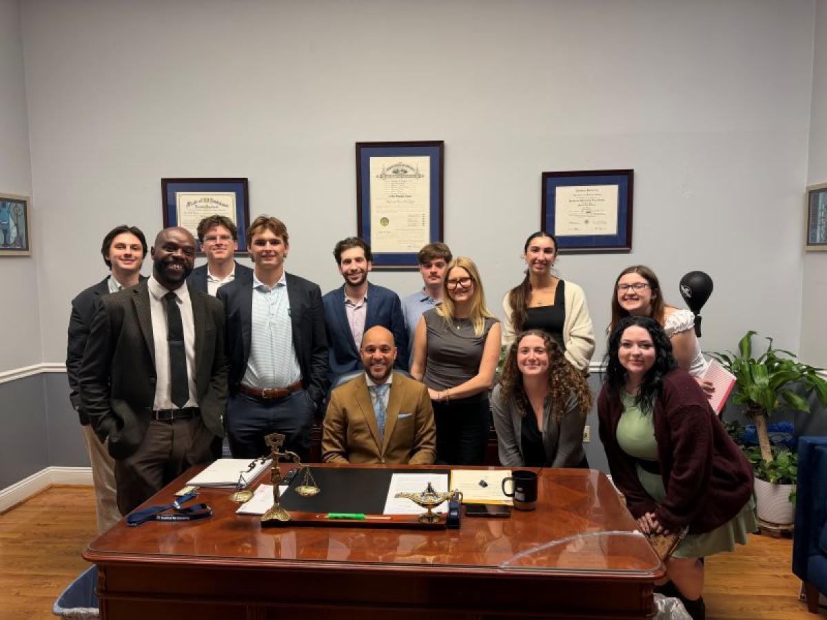 Group photo of eleven people in an office, posing for a picture behind a desk.