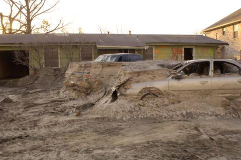 cars embedded in debris and a house damaged by Hurricane Katrina's levee breach 