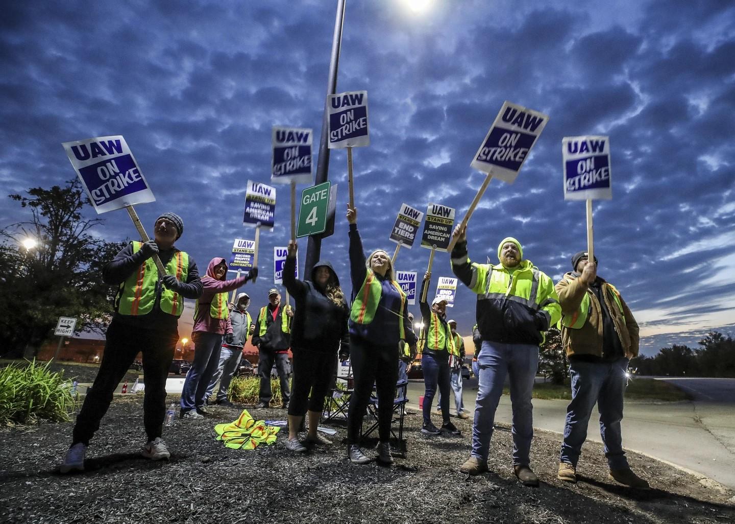 UAW workers holding signs up against an evening sky