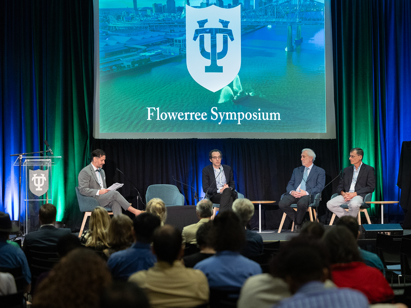 4 men seated on a podium under a screen presentation