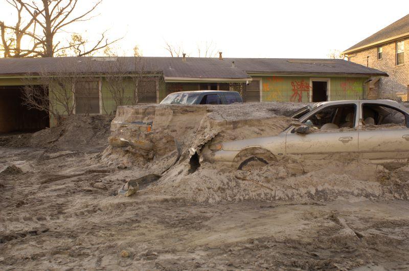 cars embedded in debris and a house damaged by Hurricane Katrina's levee breach 