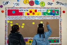 Two students point at a colorful classroom bulletin board displaying numbers.
