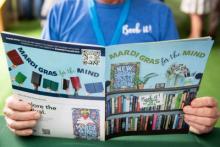 Person holds open colorful brochure about "Mardi Gras for the Mind" at a book fair.